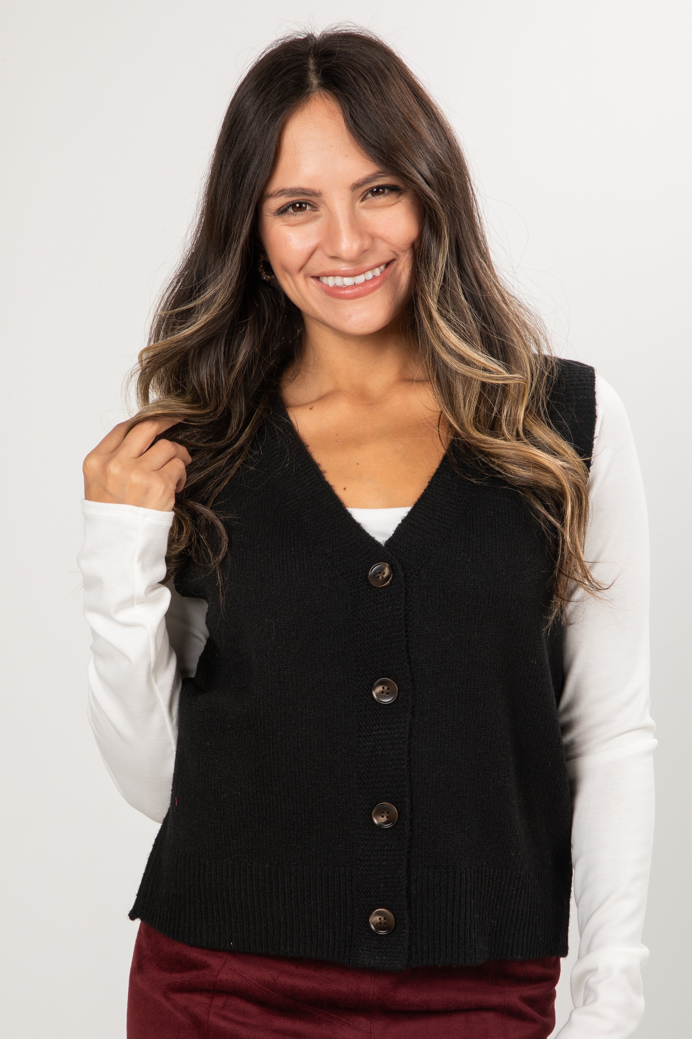 Woman wearing a black vest over a white long-sleeve shirt on a plain background