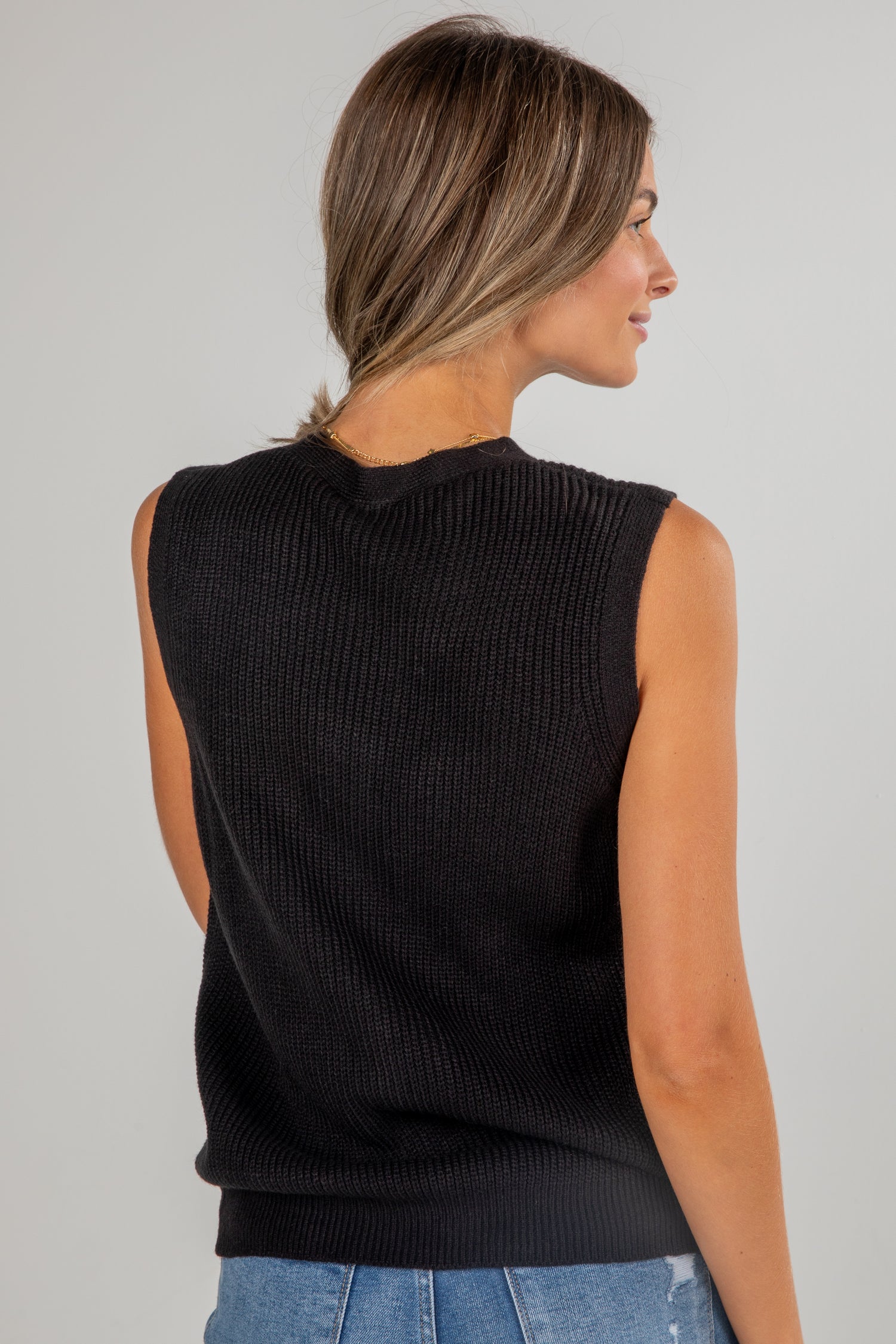 Woman wearing a black sleeveless sweater against a gray background