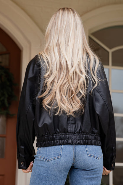 Person wearing a black jacket and blue jeans from behind, standing in front of a door.