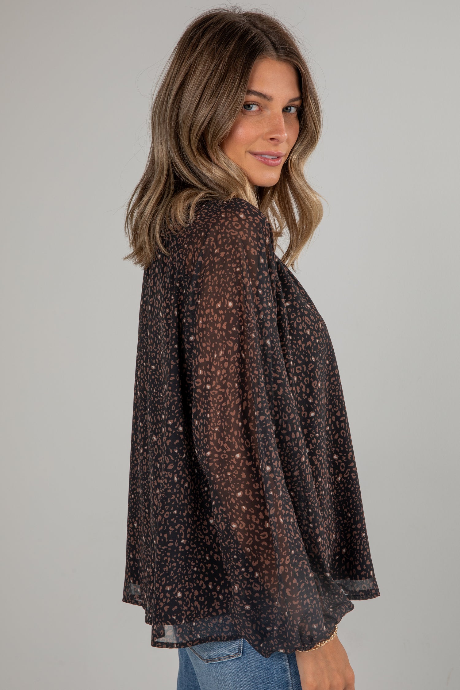 Woman wearing a sheer brown blouse with a subtle pattern on a plain background