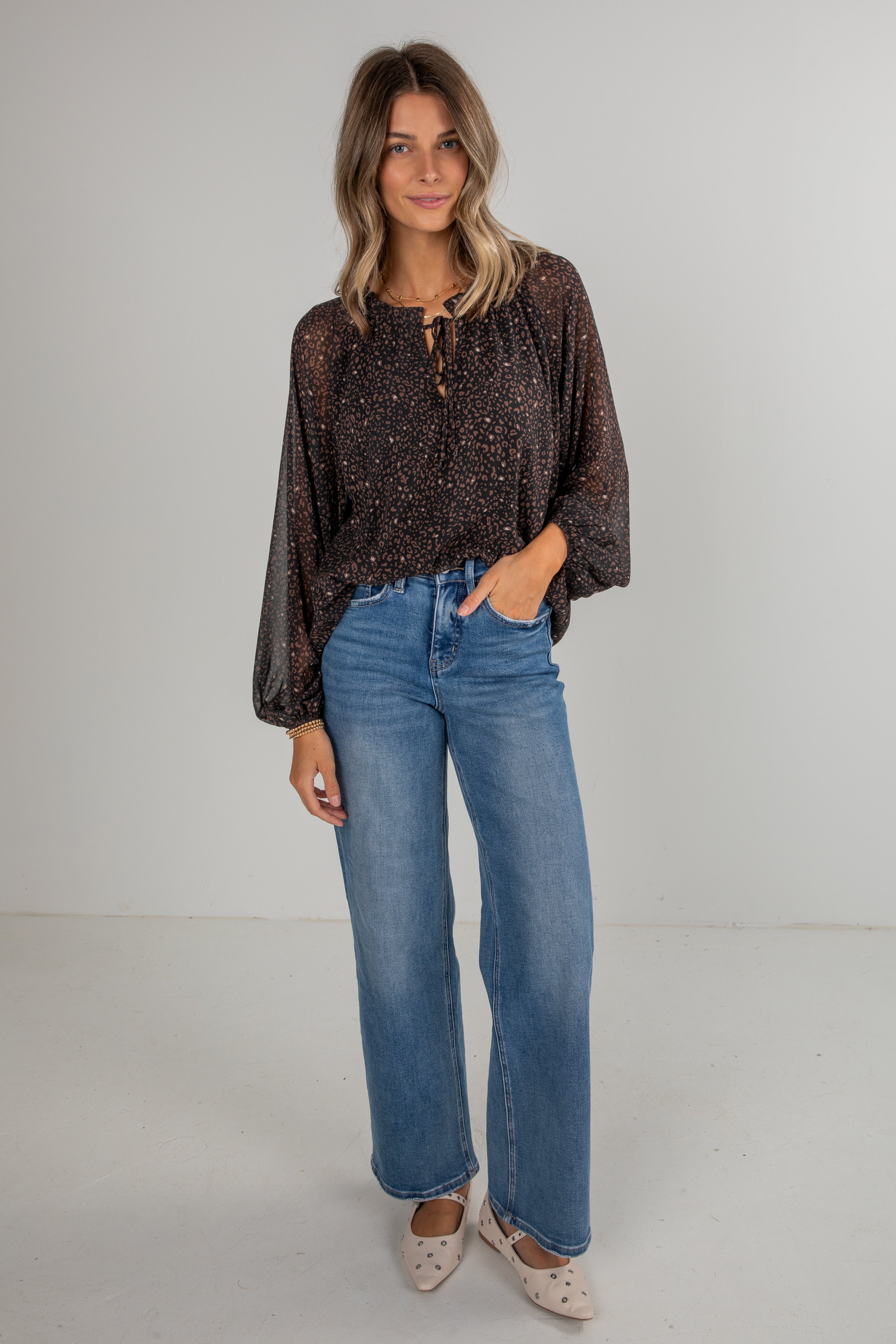 Woman wearing a patterned top and blue jeans against a plain background
