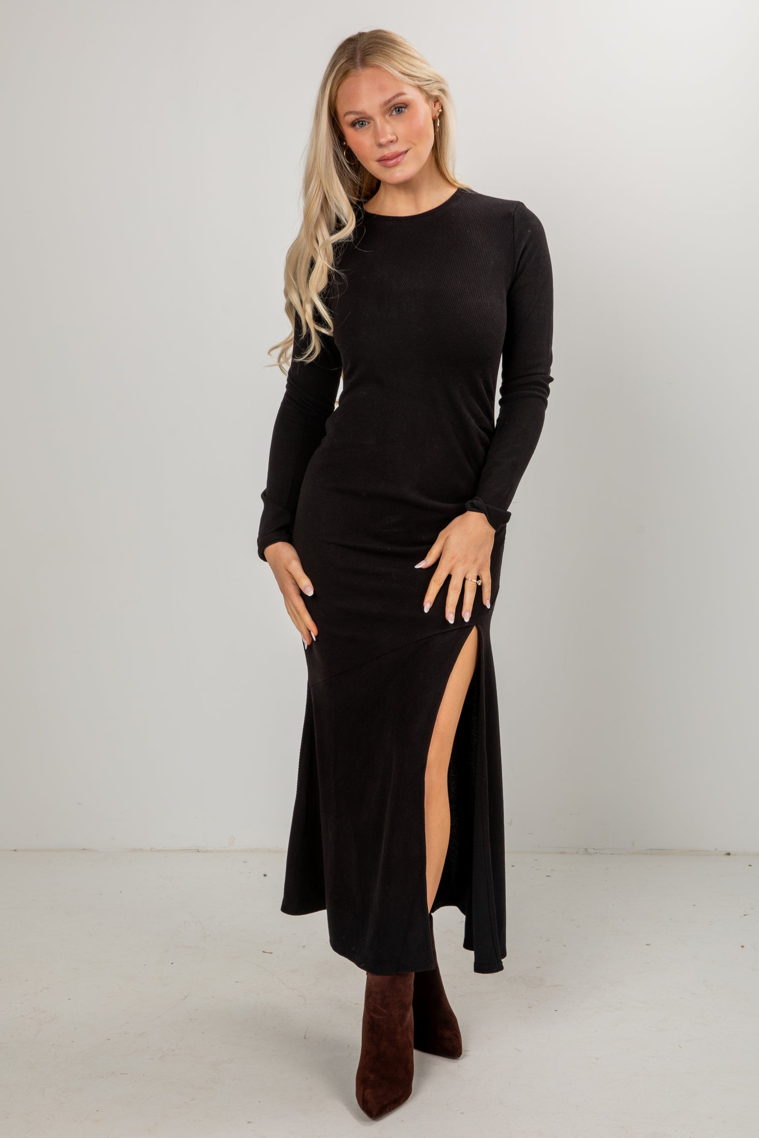 Woman wearing a black long-sleeve dress with a slit on a white background