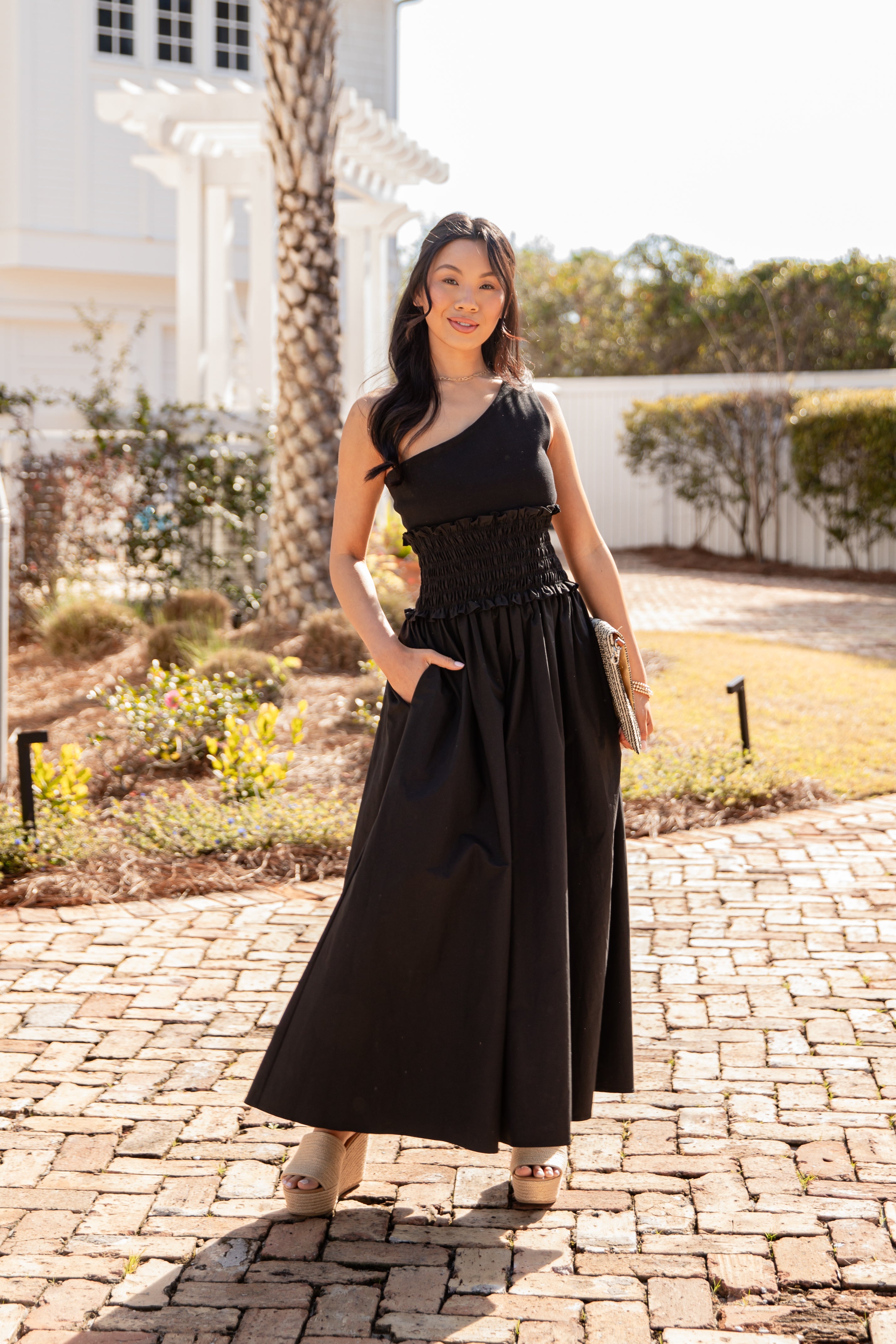 Woman in a black dress standing on a brick path with a garden background