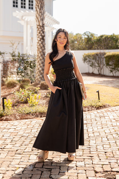 Woman in a black dress standing on a brick path with a garden background