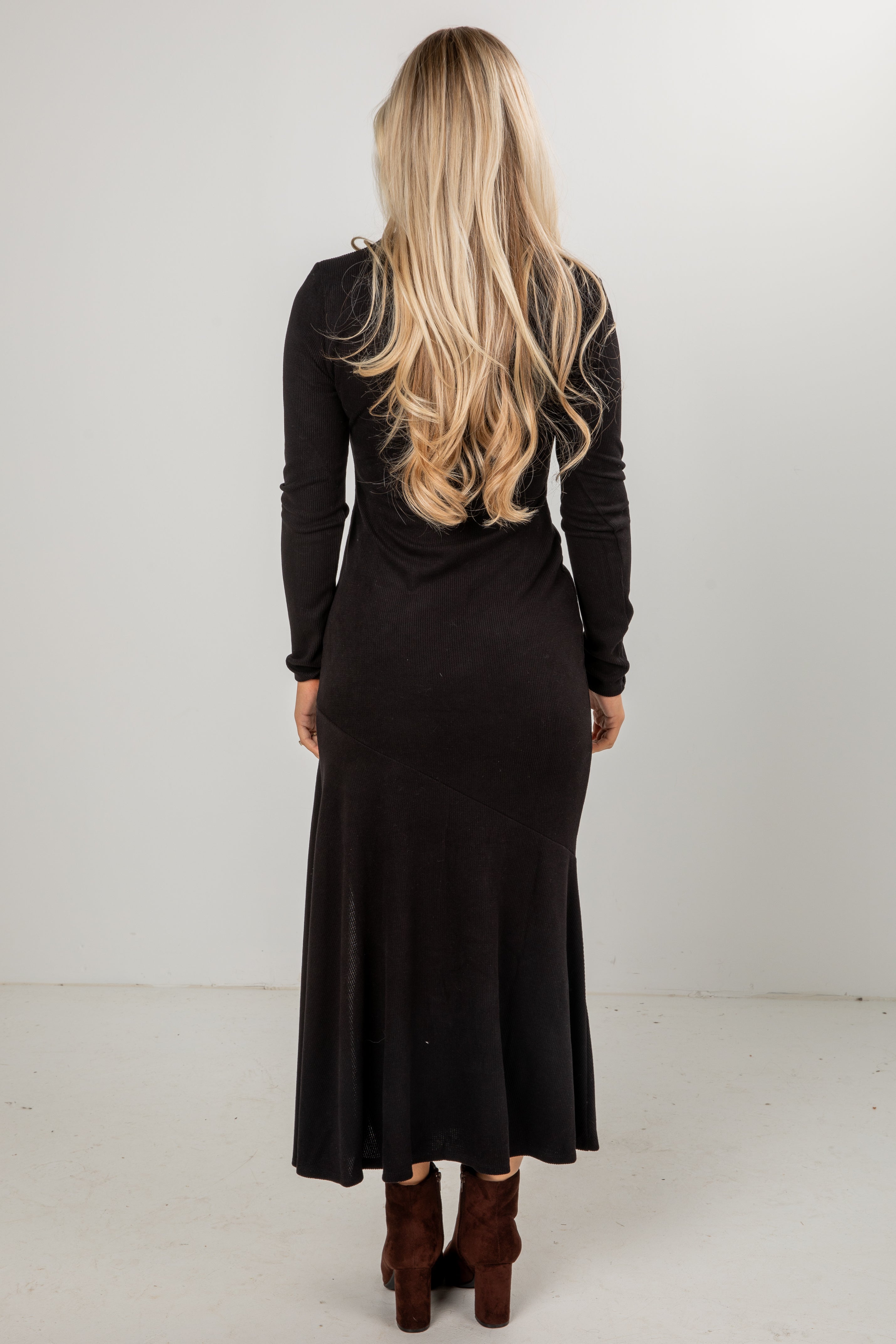 Person wearing a black dress with long sleeves and a fitted silhouette on a white background