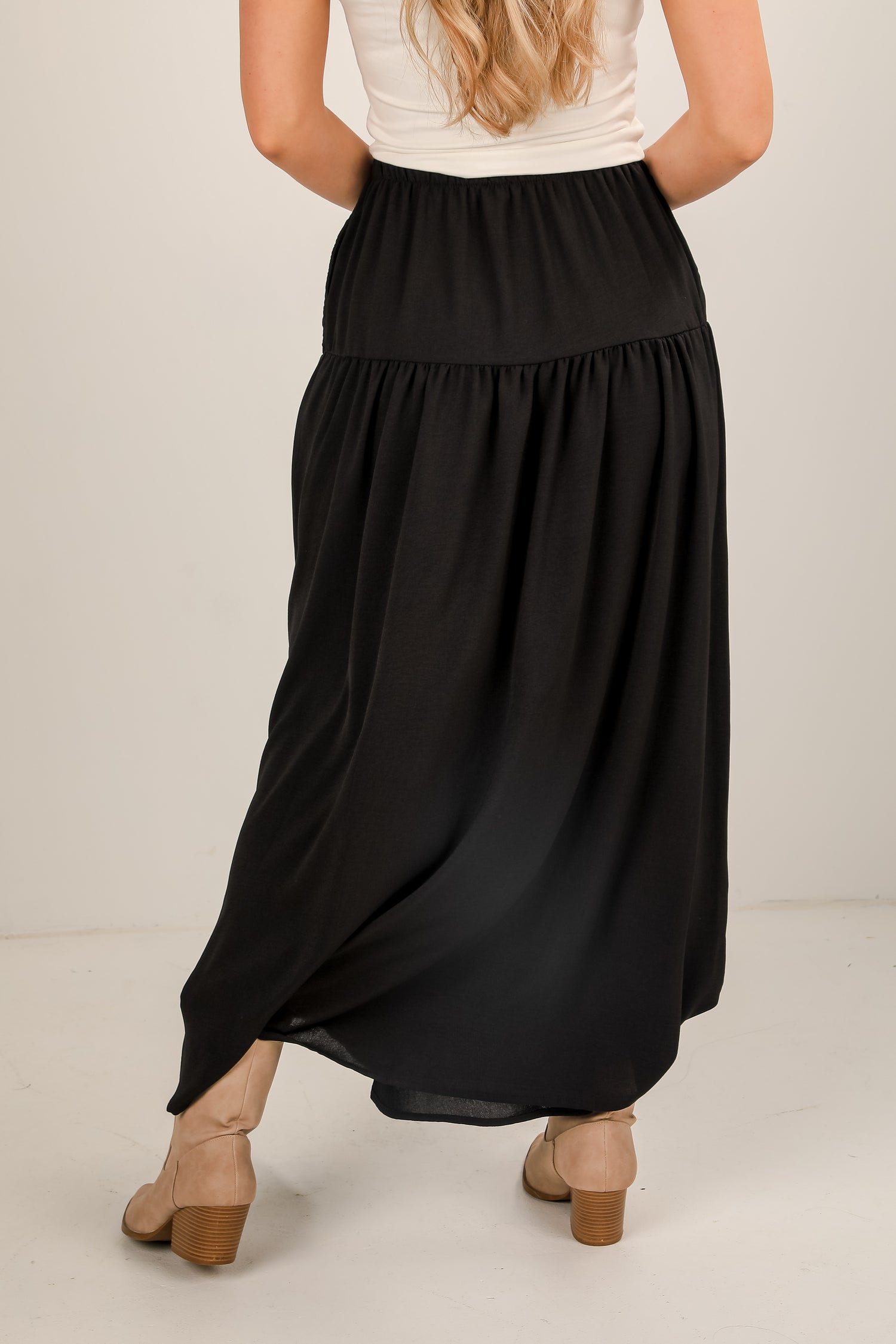 Person wearing a black skirt and beige top on a plain background