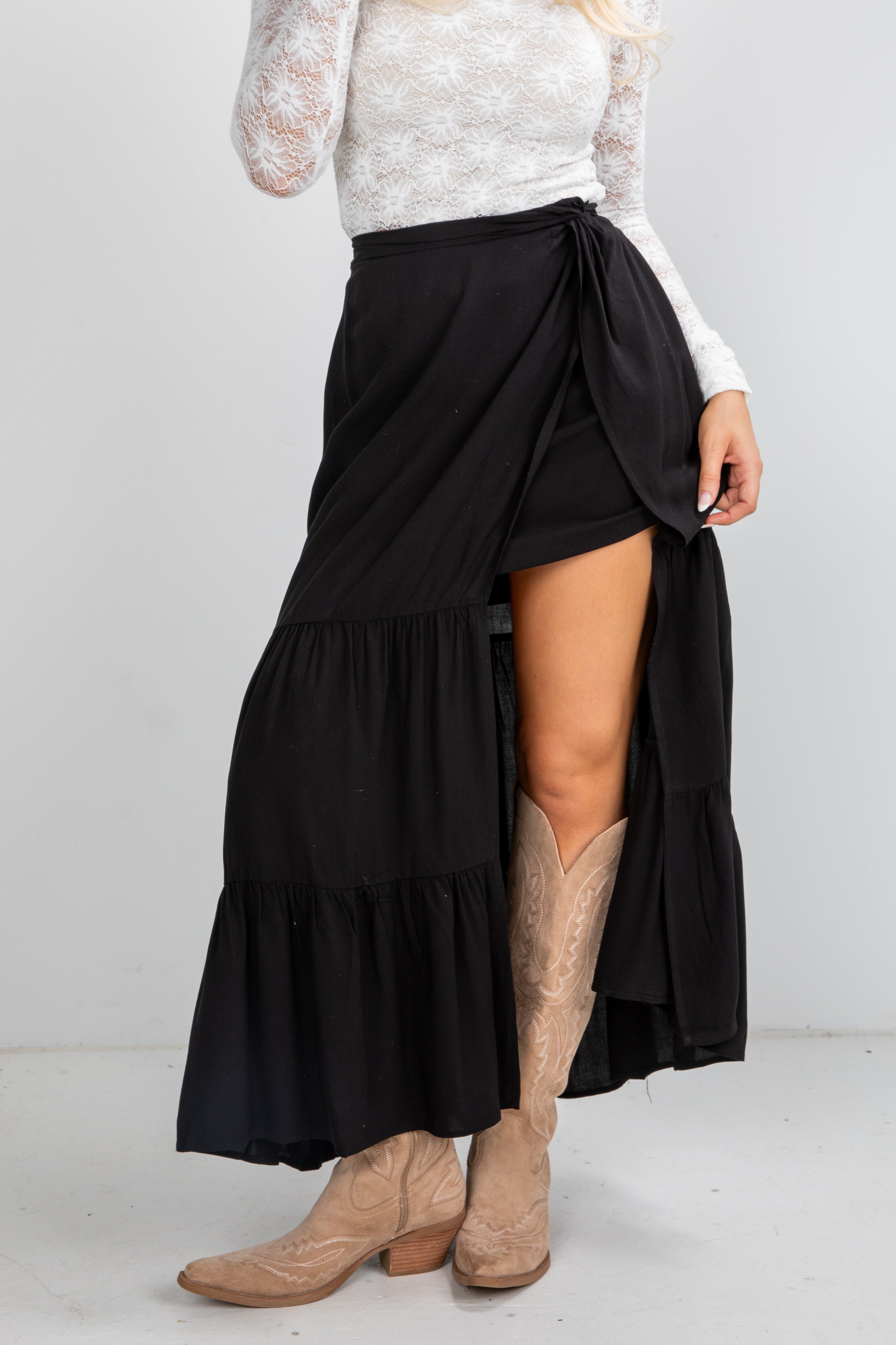 Person wearing a black tiered skirt with beige boots on a white background
