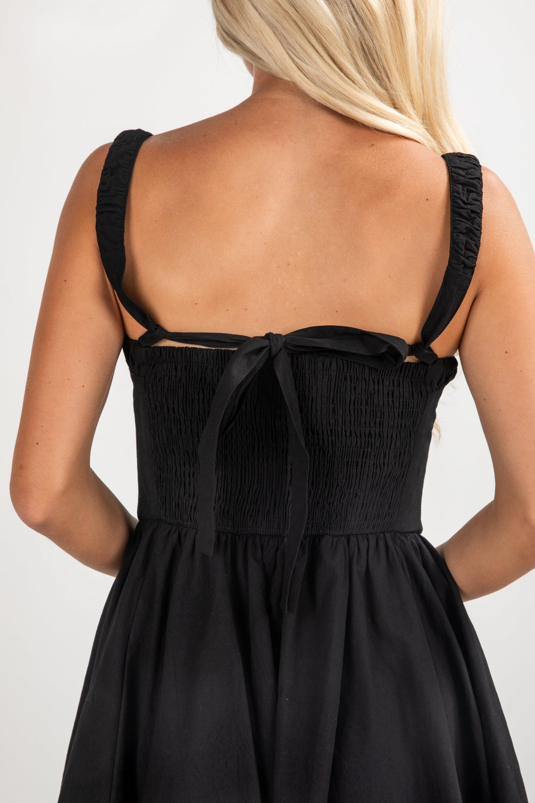 Black dress with thin straps and a bow detail on a plain background