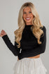 Woman wearing a black long-sleeve top and white skirt against a plain background