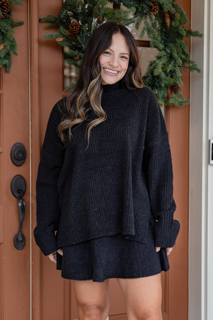 Woman wearing a dark sweater and skirt standing in front of a decorated door.