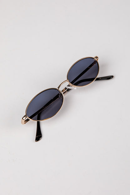 Sunglasses with gold frame and dark lenses on a light gray background