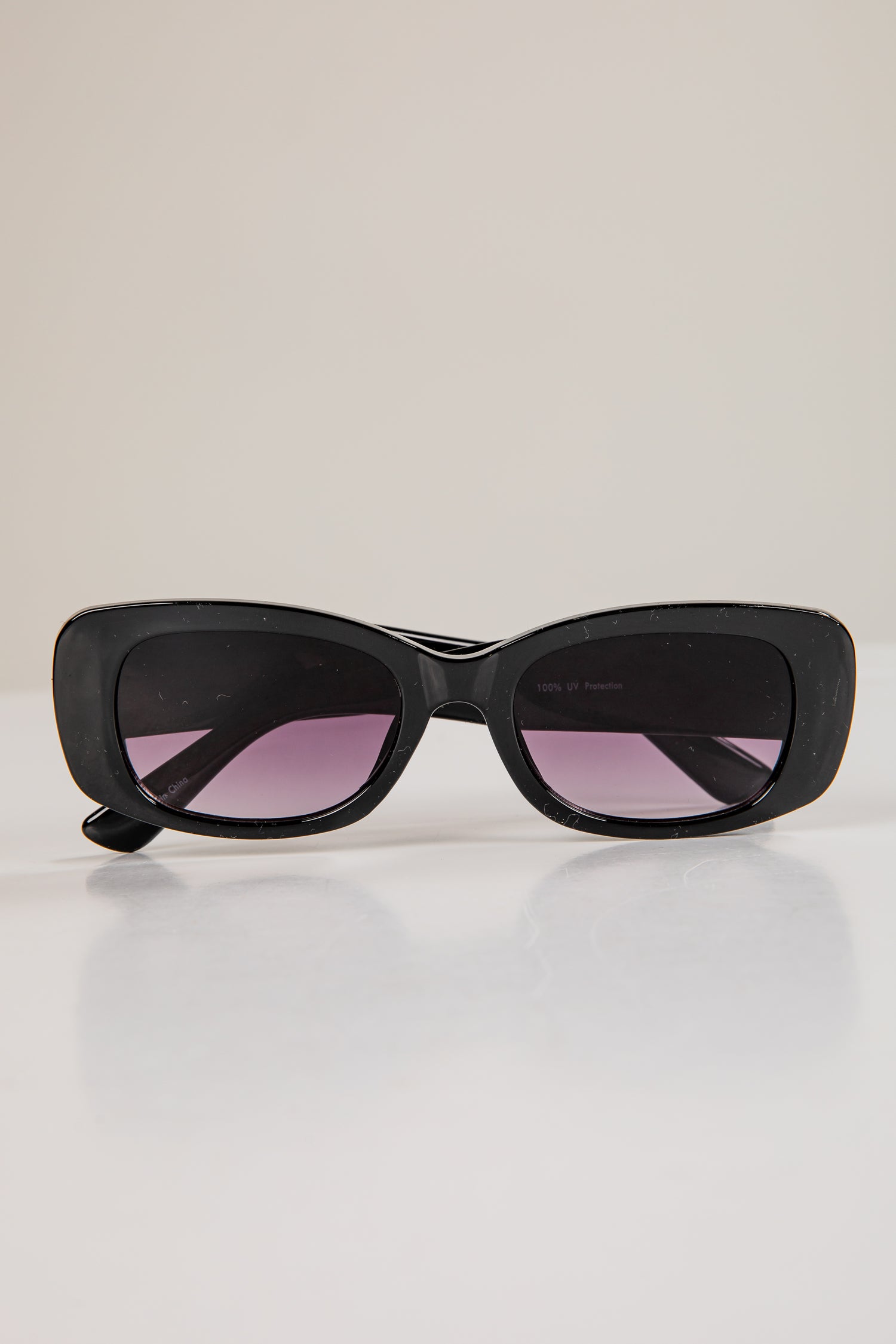 Black sunglasses with pink lenses on a light gray background