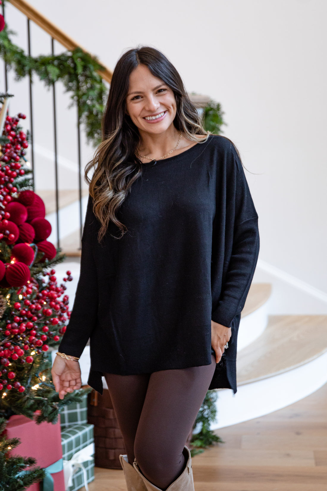 Woman wearing a black sweater standing in front of a decorated Christmas tree.
