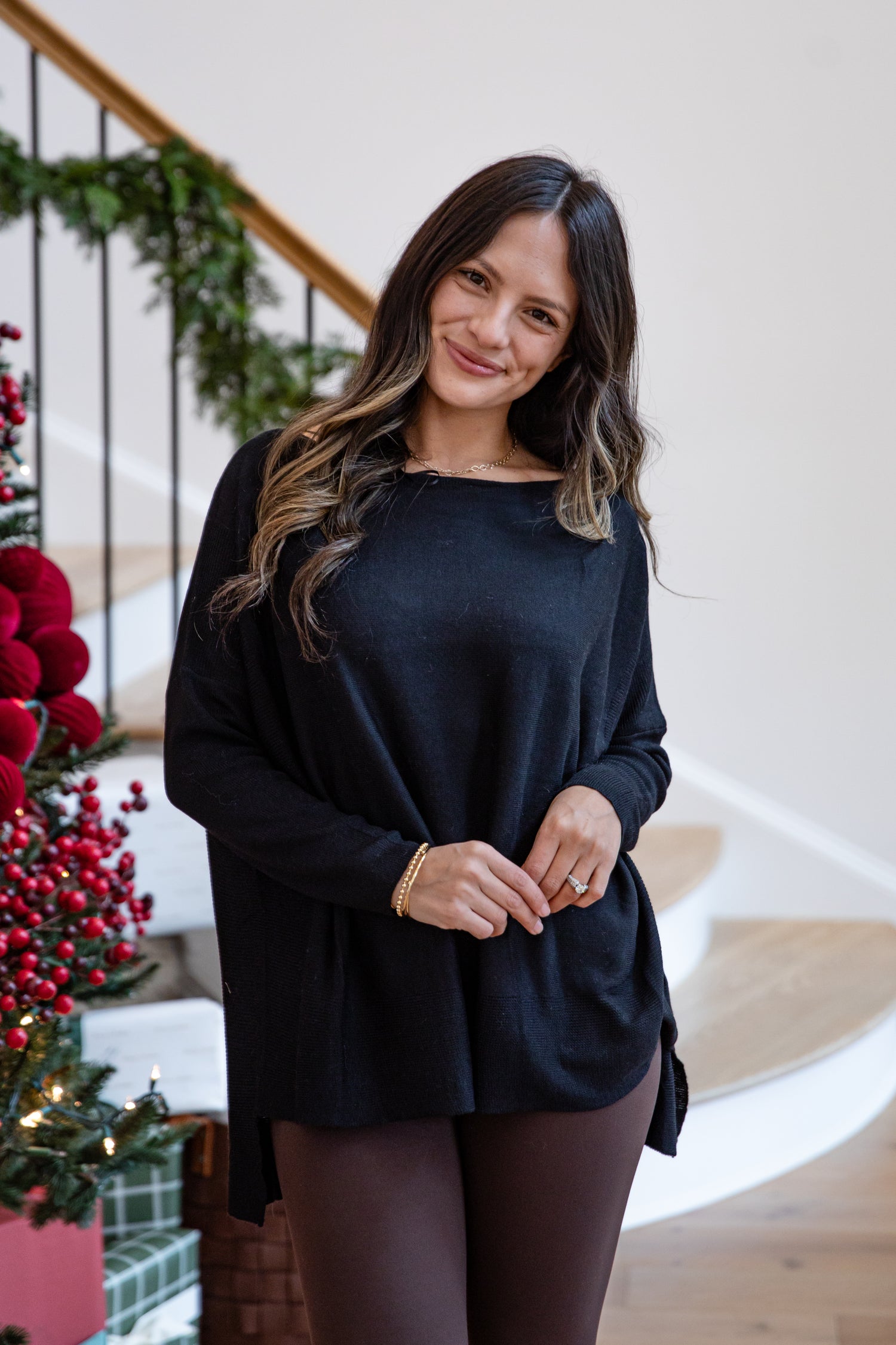 Woman in a black dress standing in a festive indoor setting with Christmas decorations.