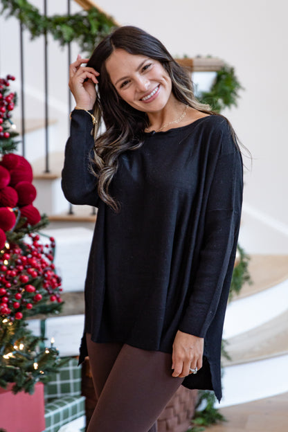 Woman wearing a black sweater standing in front of a decorated Christmas tree.