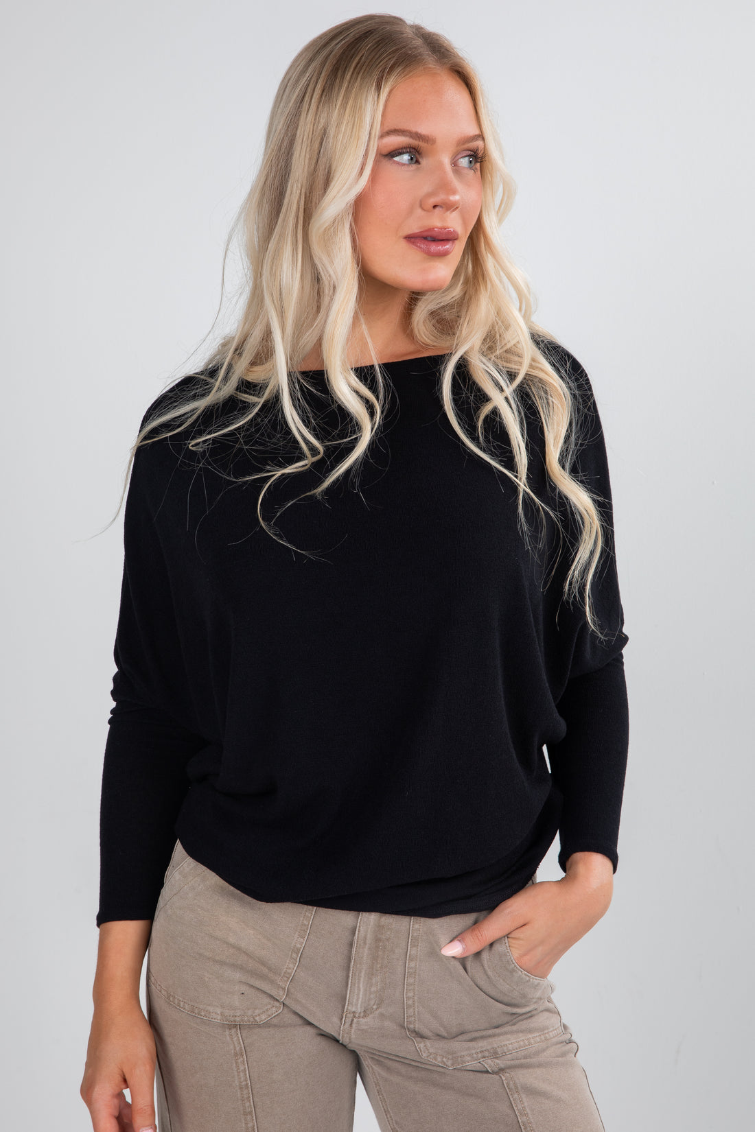 Woman wearing a black sweater and beige pants against a plain background
