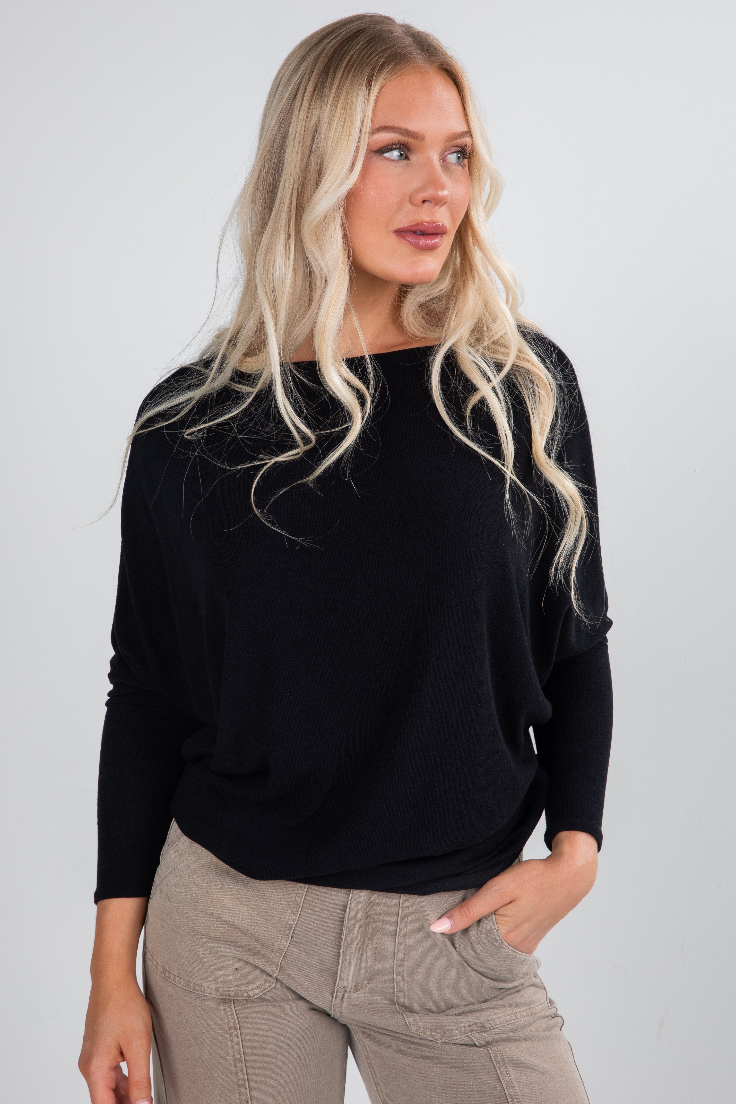 Woman wearing a black sweater and beige pants against a plain background