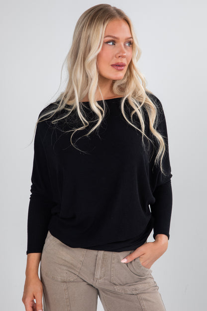 Woman wearing a black sweater and beige pants against a plain background