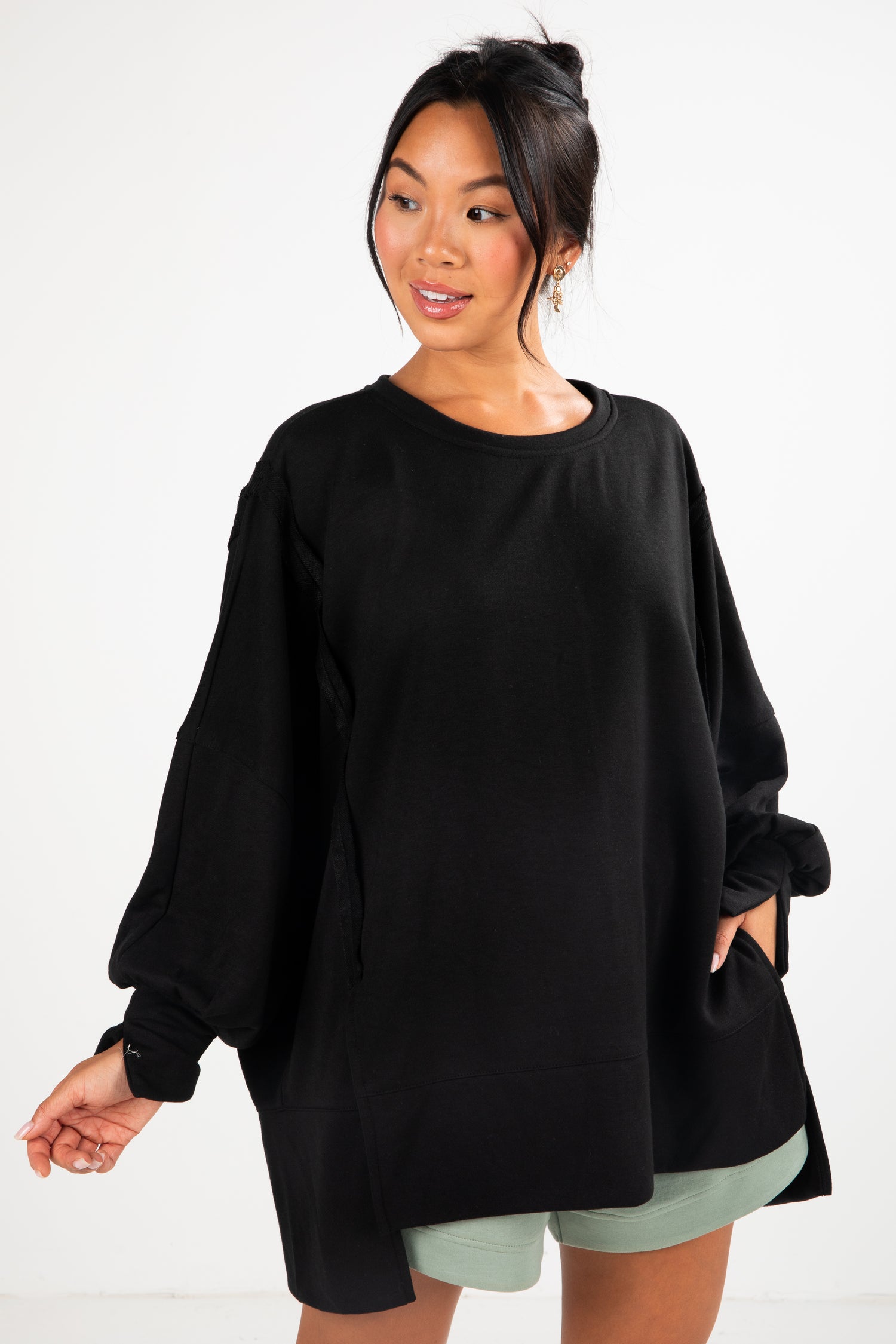 Woman wearing a black oversized sweater with green shorts on a white background