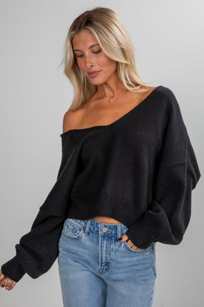 Woman wearing a black off-shoulder sweater and blue jeans on a gray background