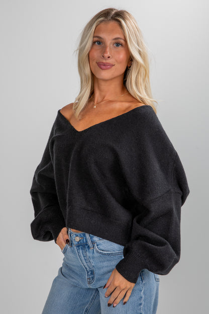 Woman wearing a black off-shoulder sweater and blue jeans on a gray background