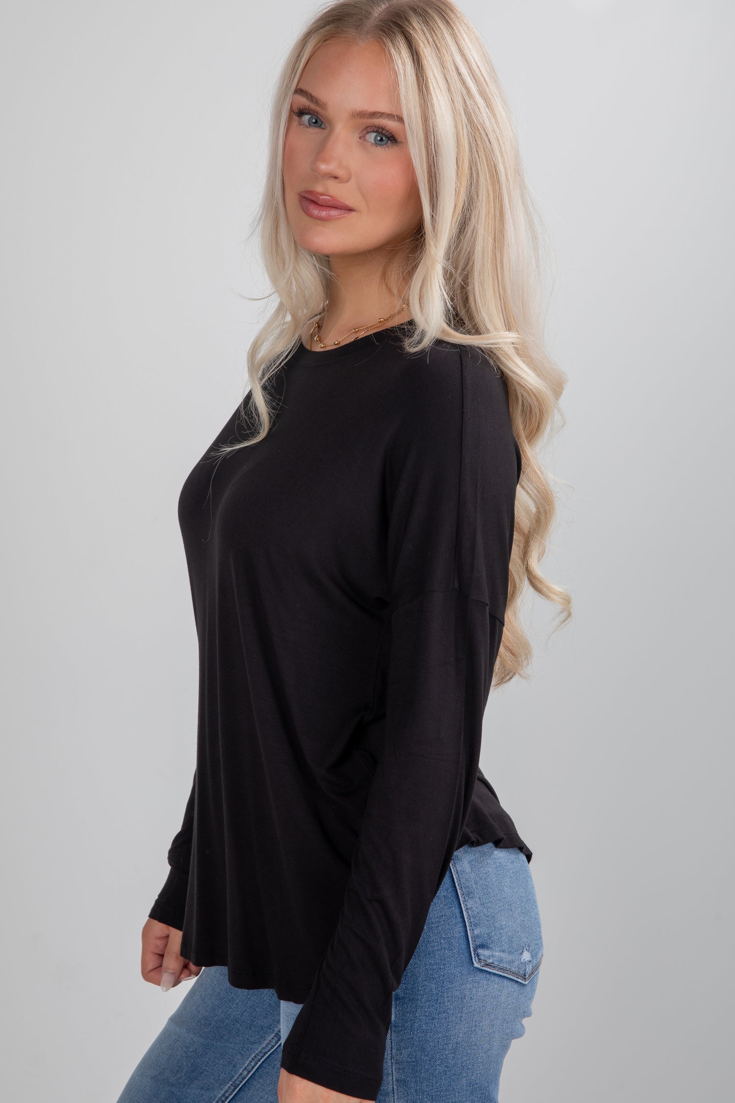 Woman wearing a black long-sleeve top and blue jeans on a gray background