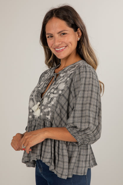 Woman wearing a plaid blouse with floral details on a plain background