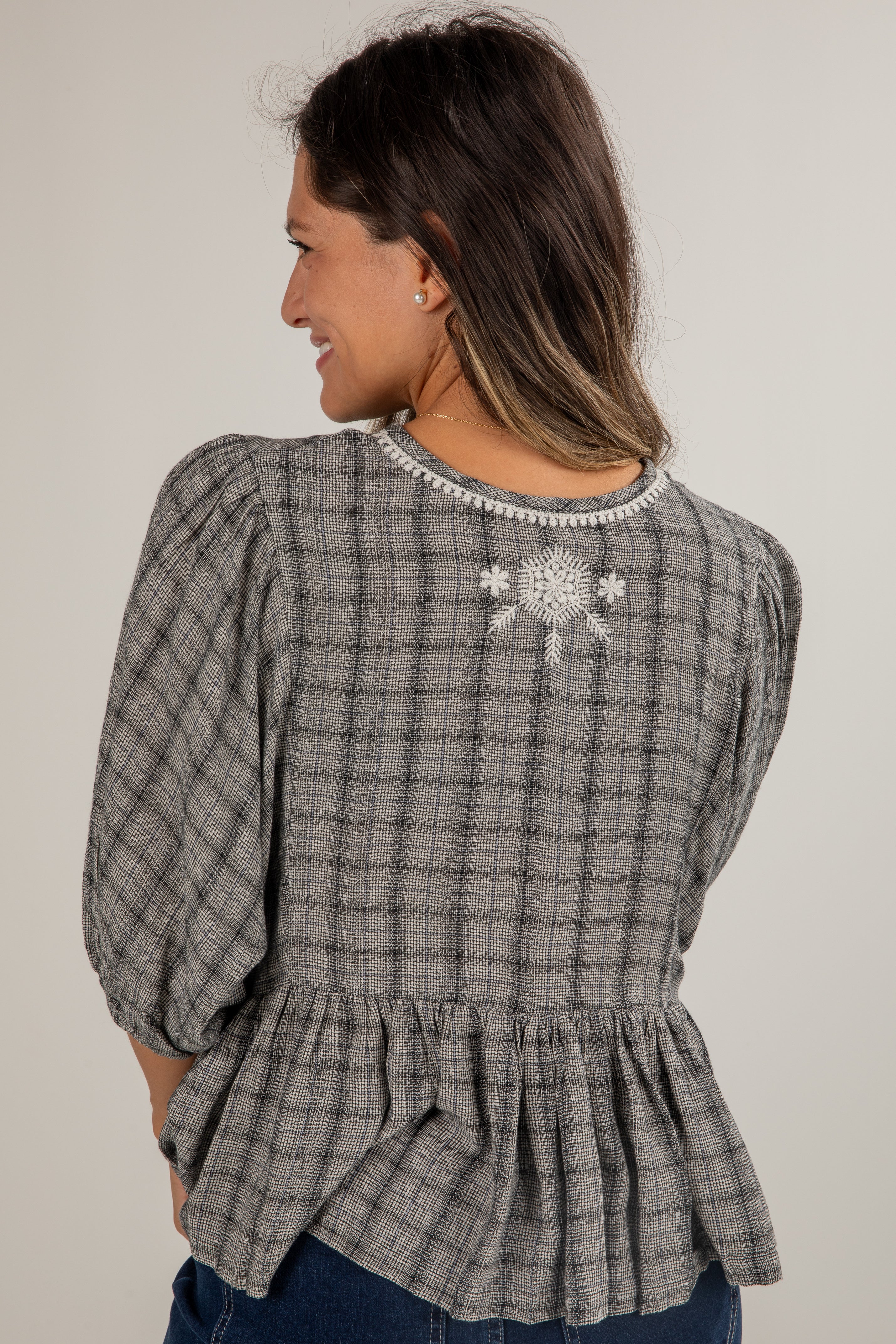 Woman wearing a plaid blouse with a snowflake design on a plain background