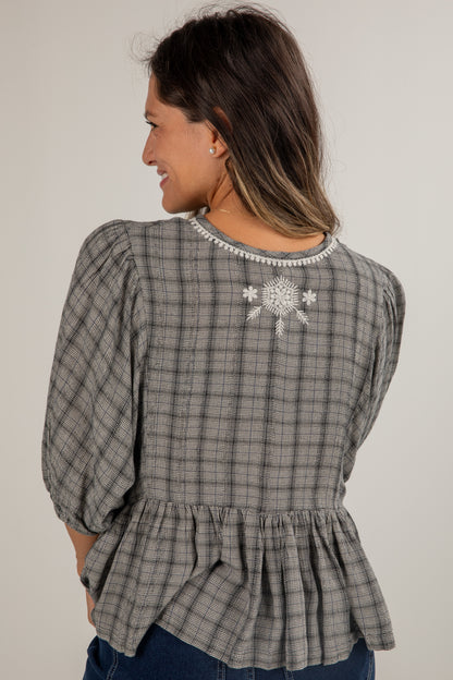 Woman wearing a plaid blouse with a snowflake design on a plain background