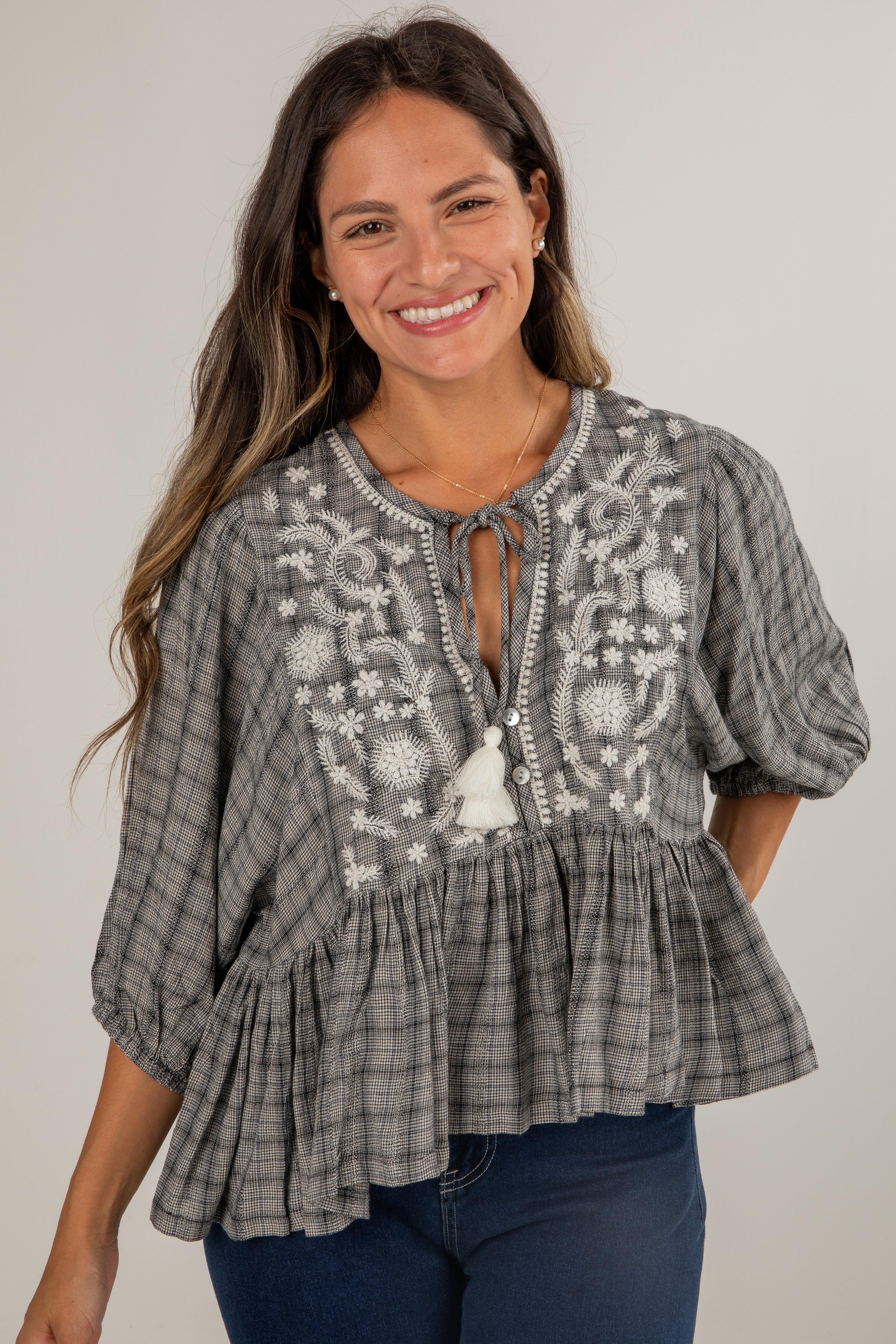 Woman wearing a gray embroidered blouse with blue jeans on a plain background