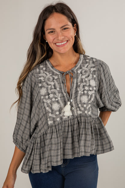 Woman wearing a gray embroidered blouse with blue jeans on a plain background