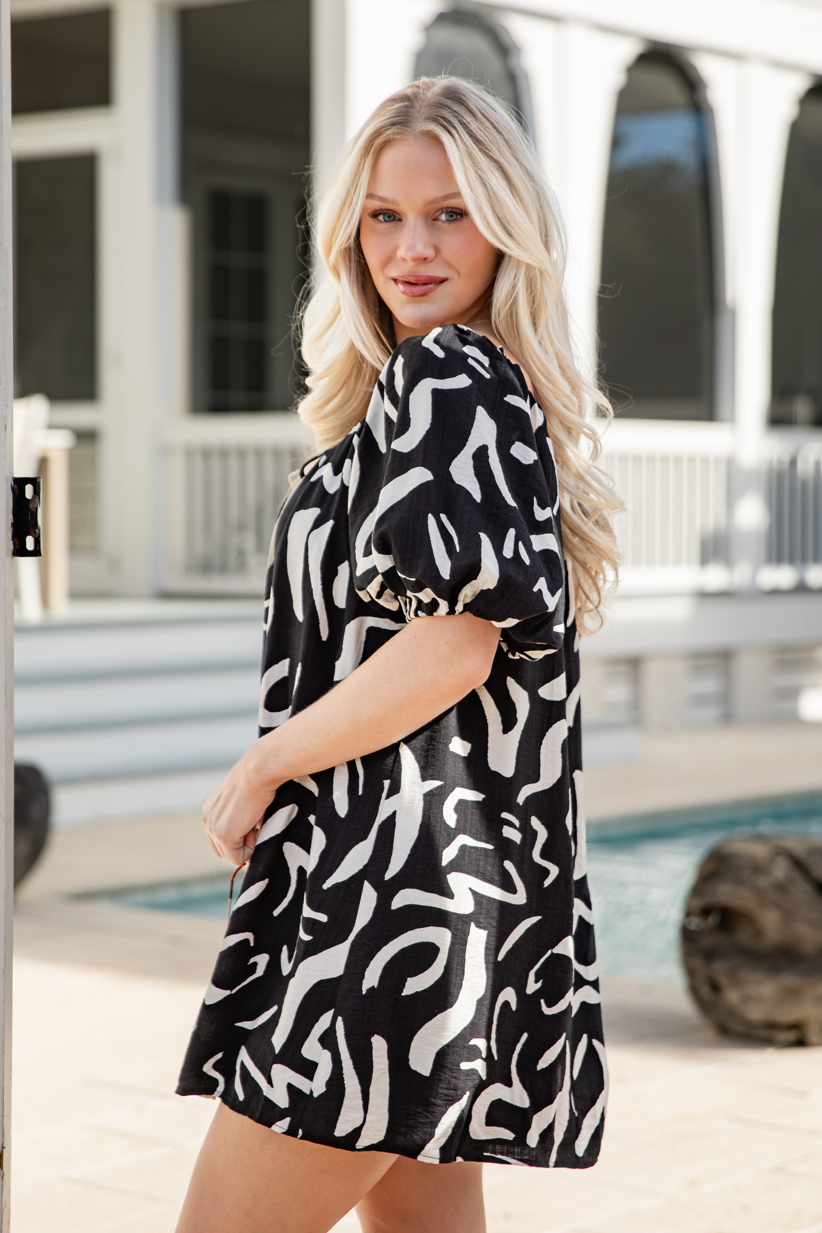 Woman wearing a black and white patterned dress by a pool.