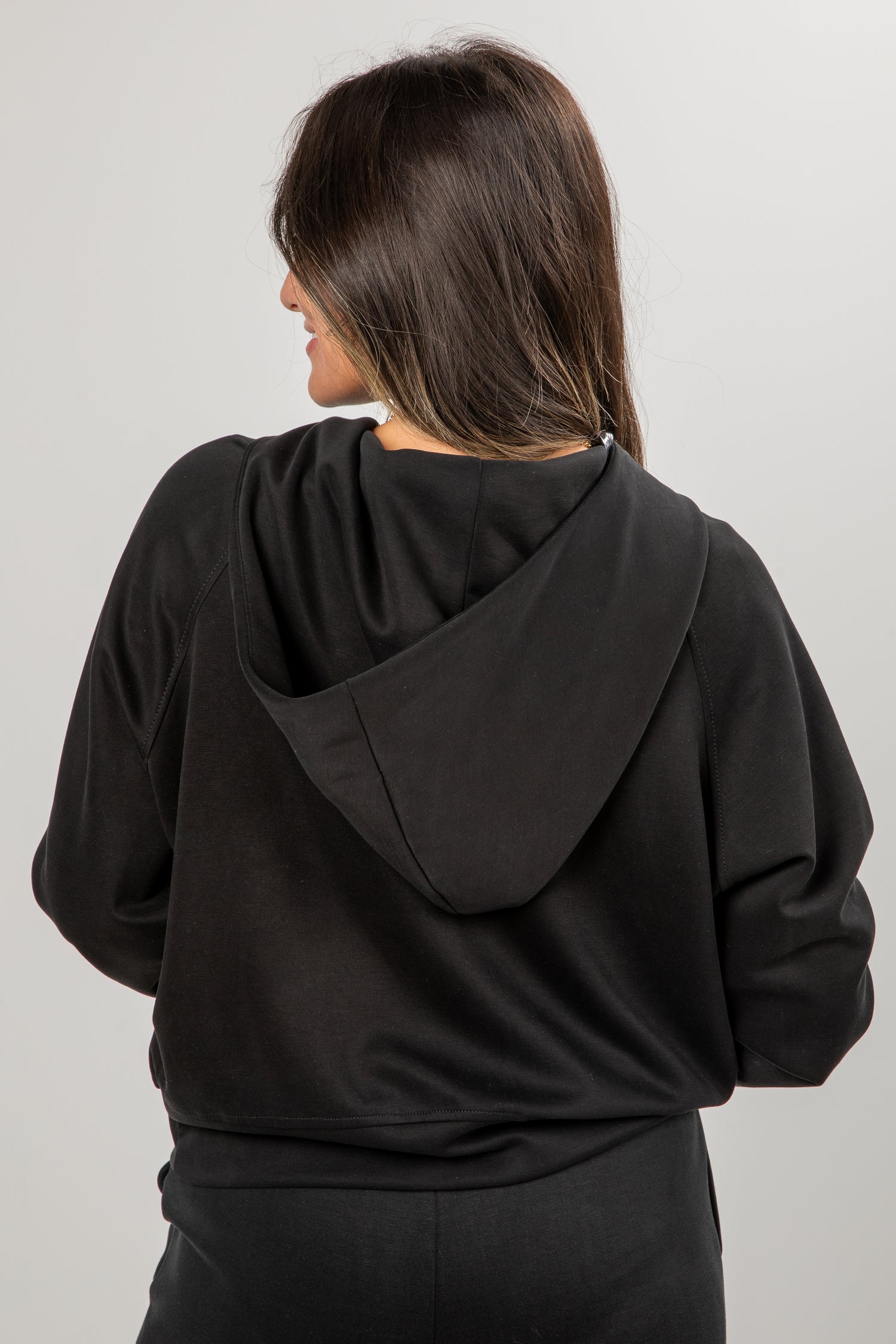 Person wearing a black hoodie from behind on a plain background