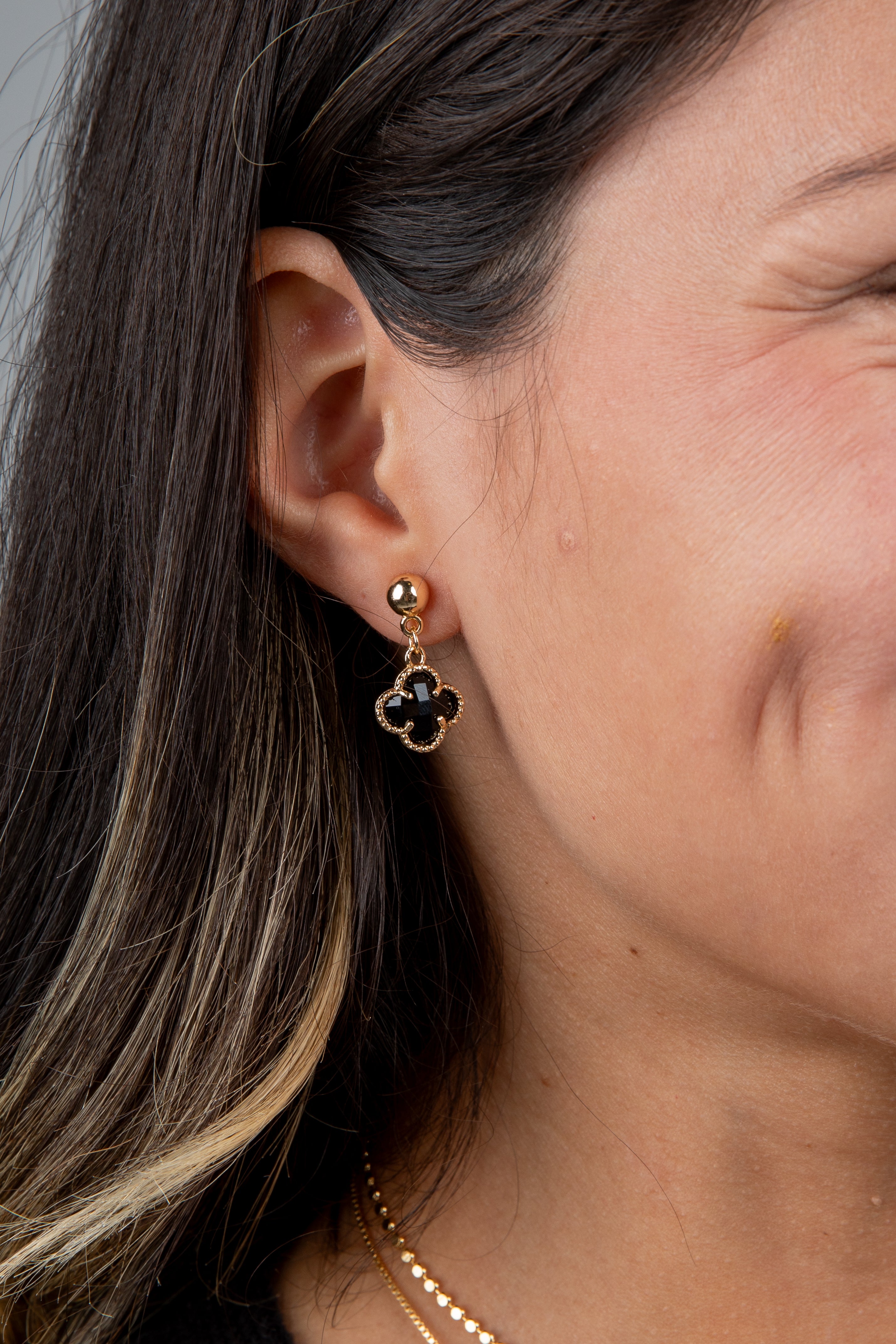 Close-up of a person wearing a gold and black clover-shaped earring.