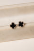 Black clover-shaped earrings on a beige surface