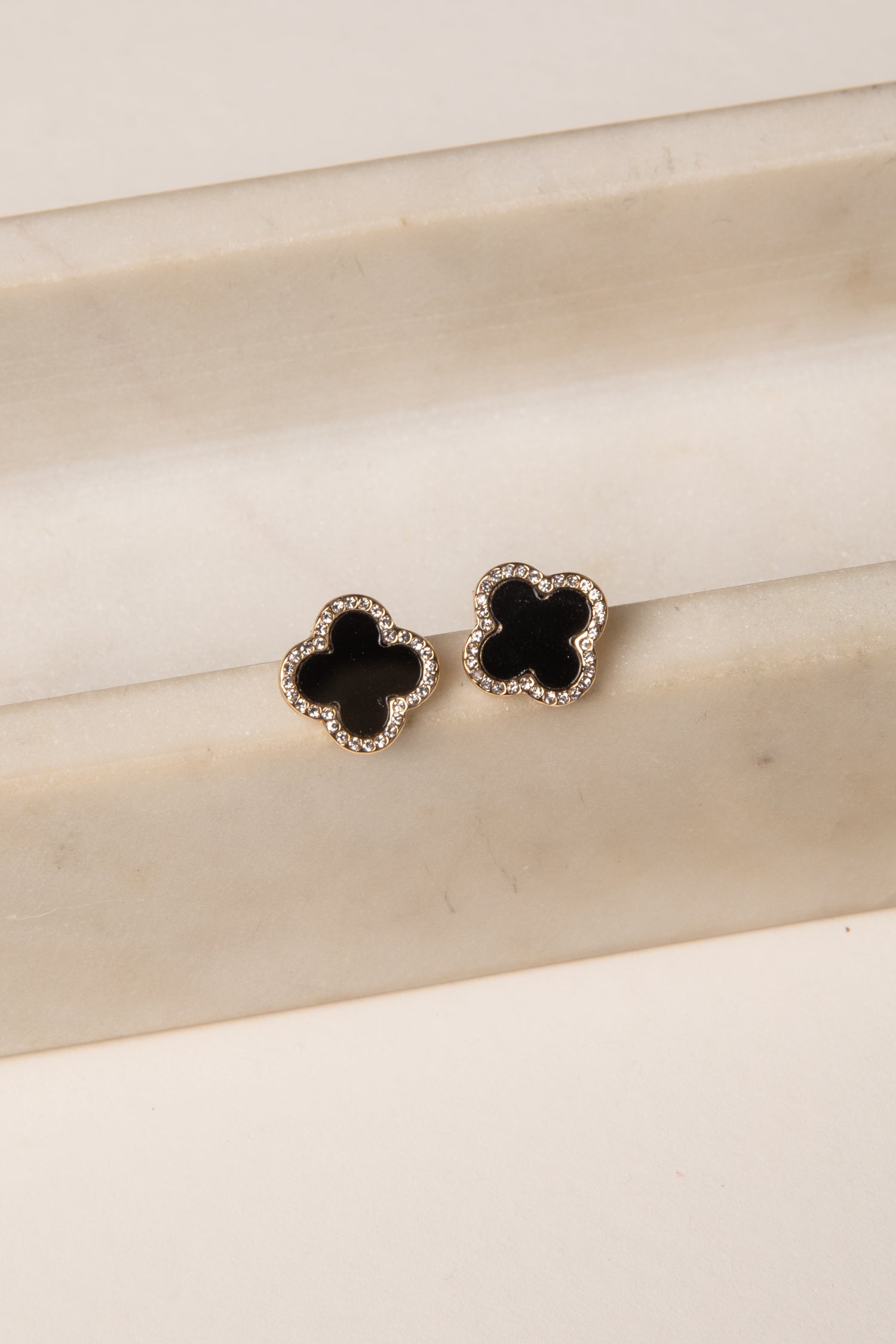 Pair of black flower-shaped earrings on a beige surface