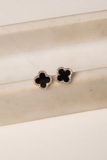 Pair of black flower-shaped earrings on a beige surface