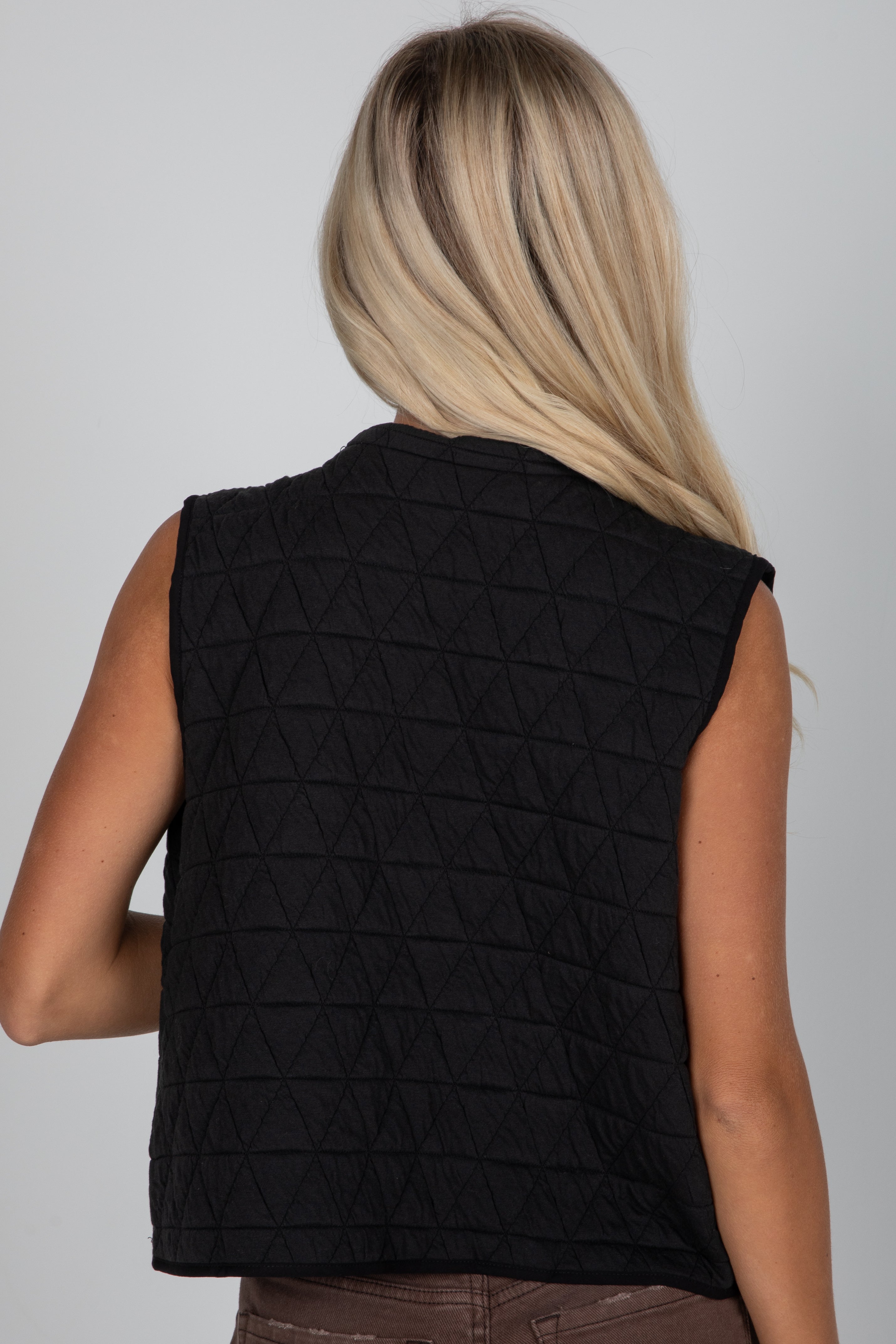 Person wearing a black quilted vest on a plain background