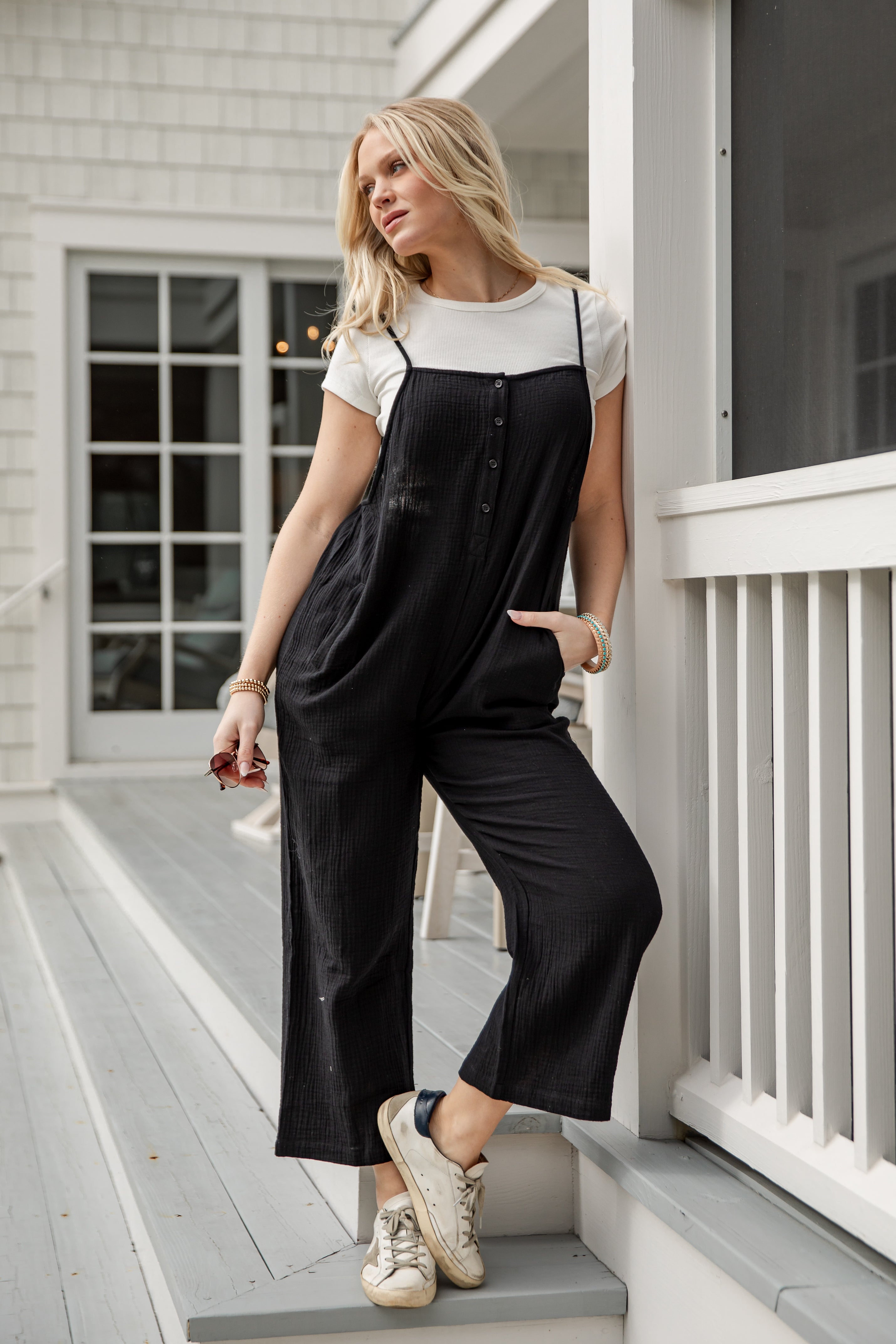 Woman wearing a black jumpsuit and white sneakers on a porch.