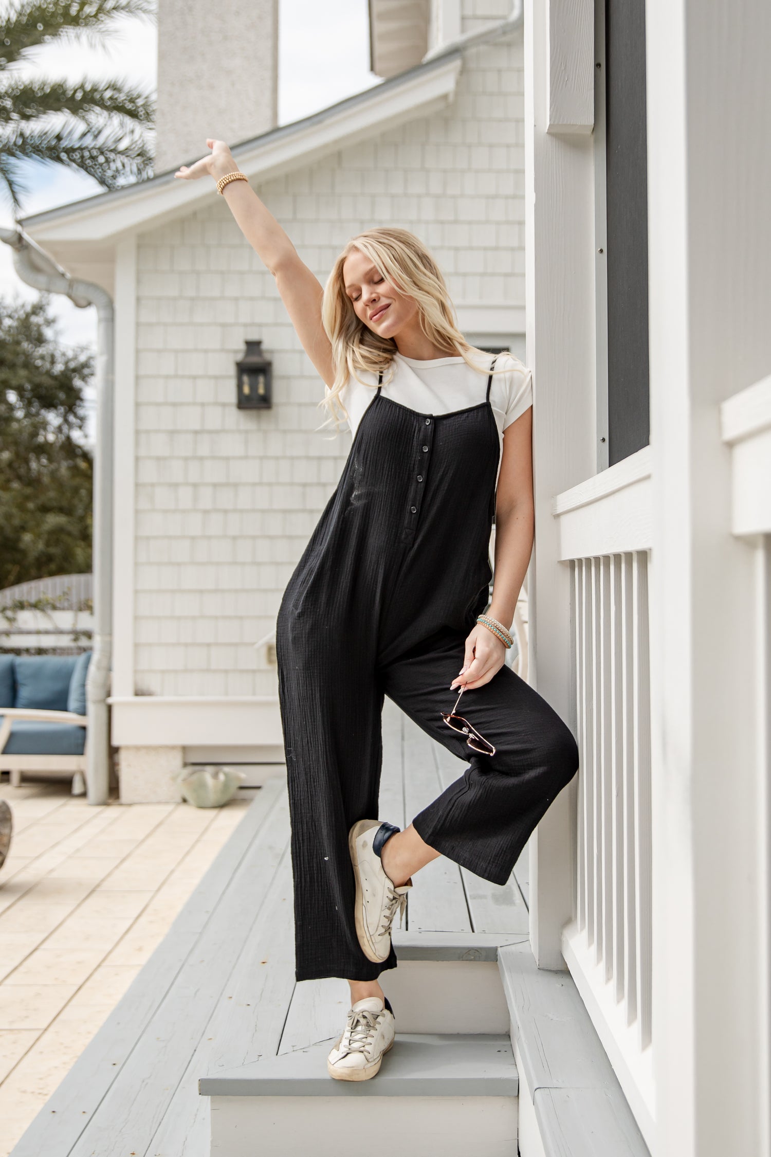 Woman in a black jumpsuit standing on a porch of a house.