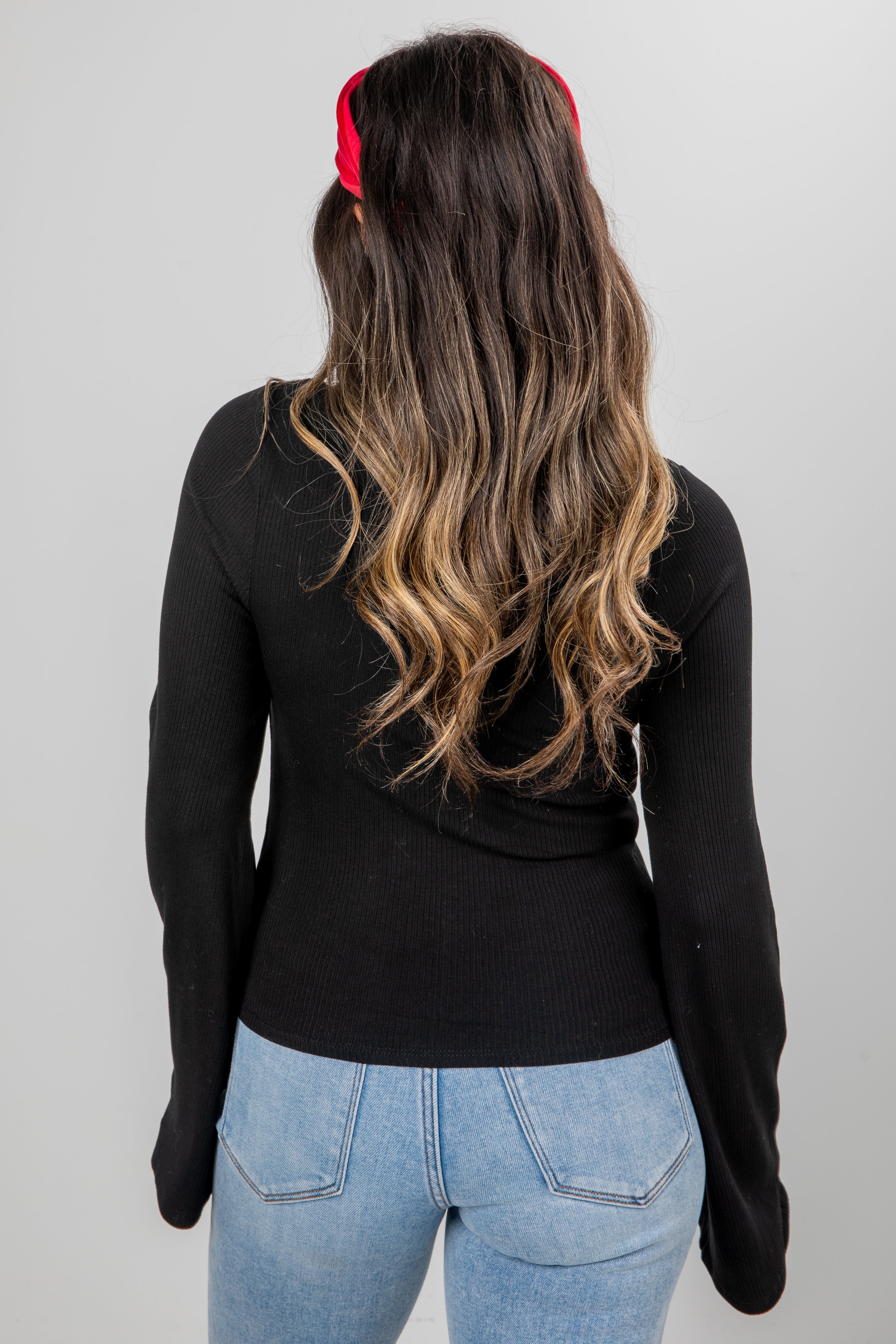 Person wearing a black long-sleeve top and blue jeans with a red headband on a plain background