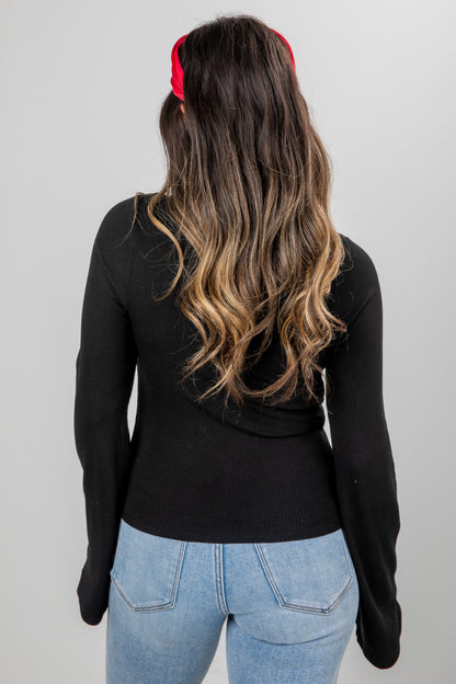 Person wearing a black long-sleeve top and blue jeans with a red headband on a plain background