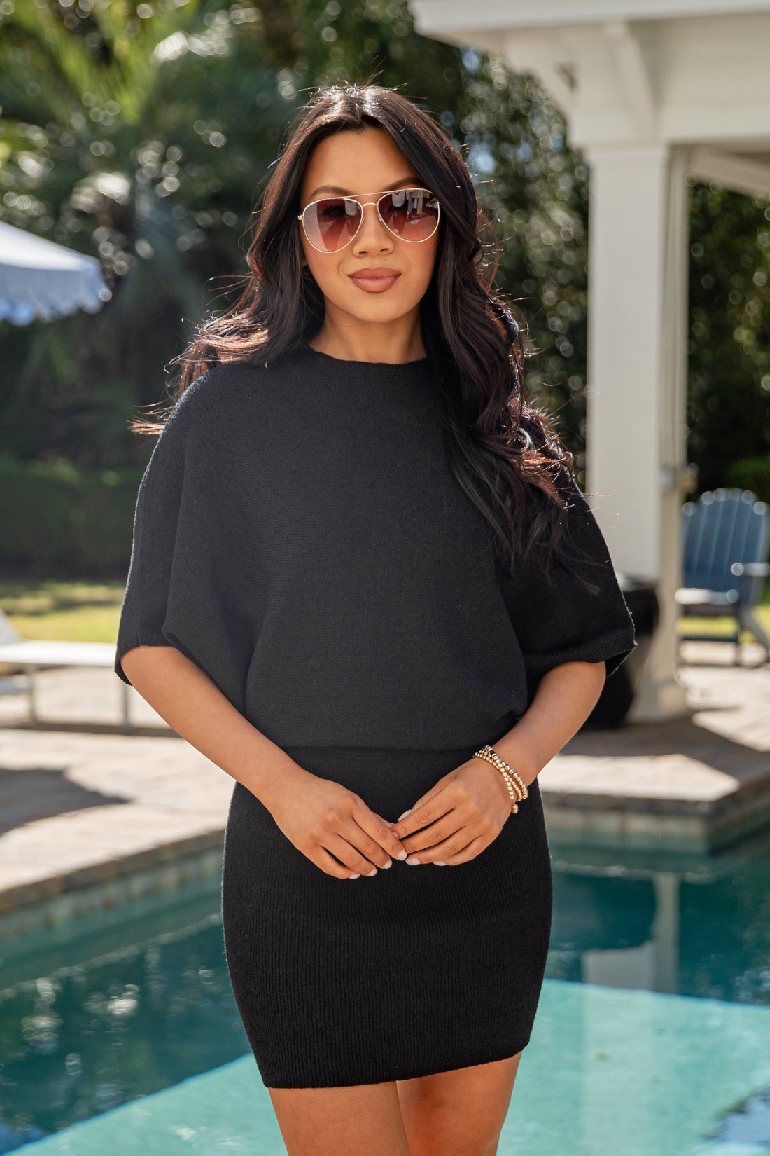Woman in a black outfit standing by a pool with sunglasses on
