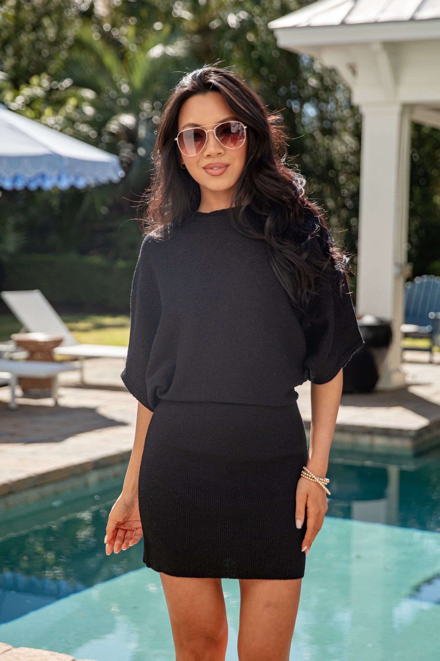 Woman in a black outfit standing by a pool with sunglasses on
