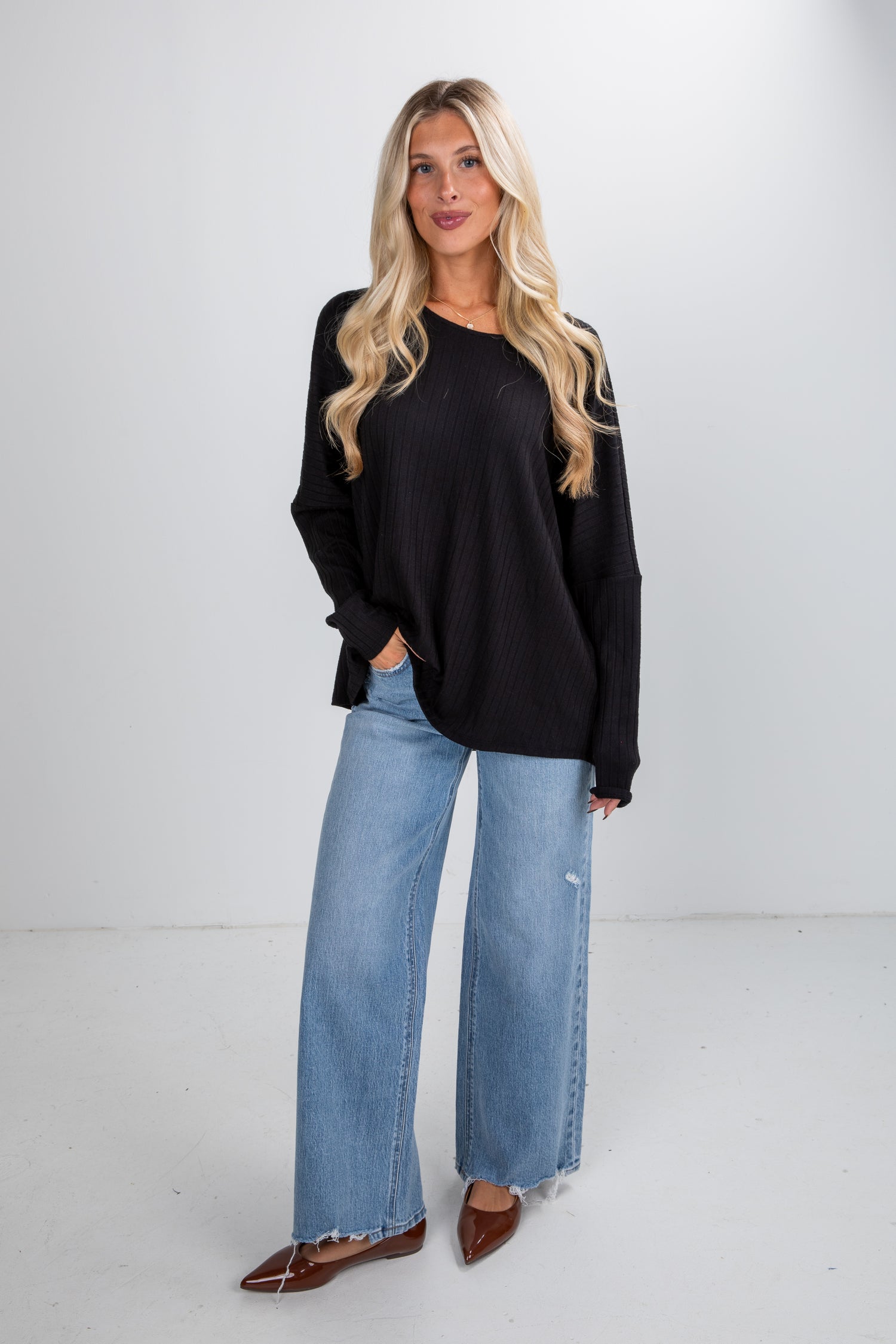 Woman wearing a black long-sleeve top and blue jeans on a white background