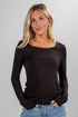 Woman wearing a black long-sleeve top and blue jeans against a gray background