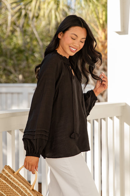 Woman in a black blouse and white pants standing on a porch.
