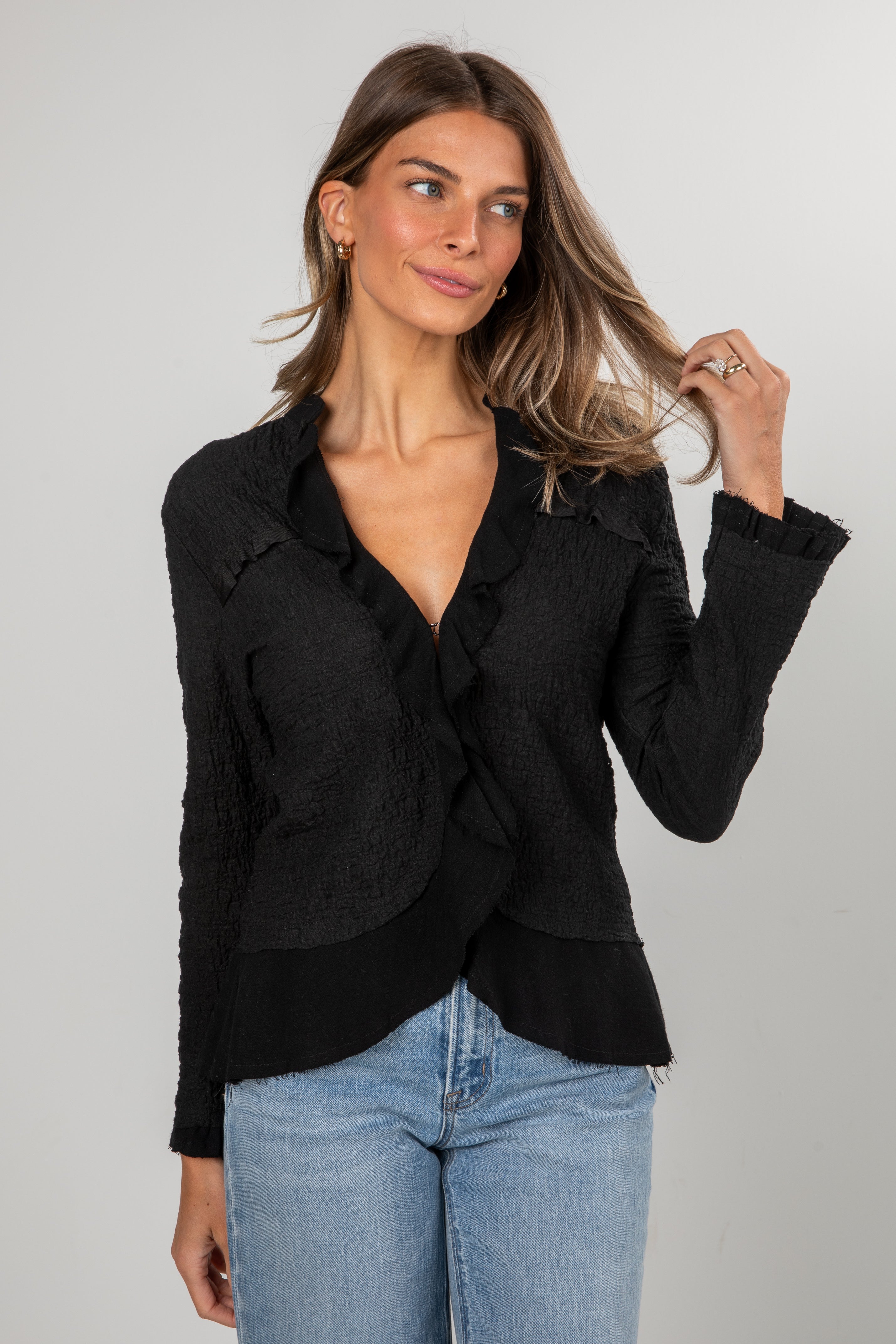 Woman wearing a black blazer and blue jeans against a gray background