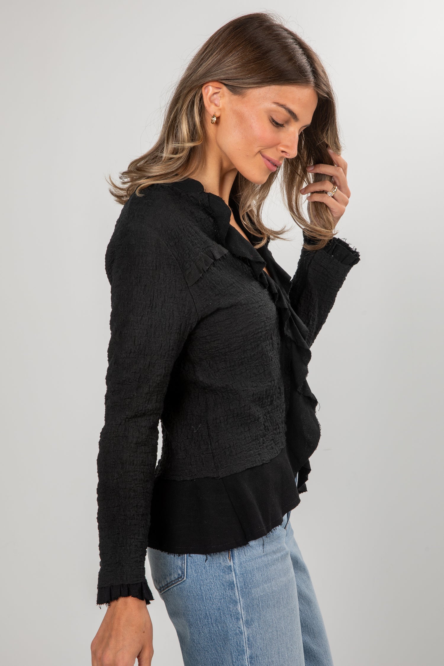 Woman wearing a black jacket with ruffled details on a plain background