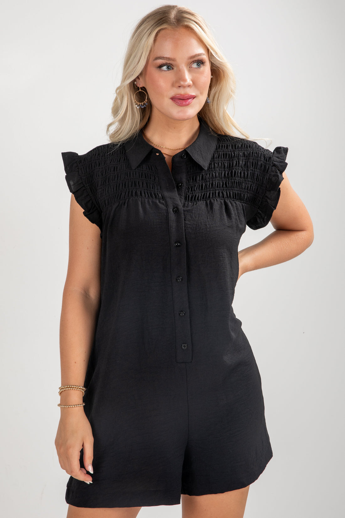 Woman wearing a black romper with ruffled collar and sleeves on a plain background